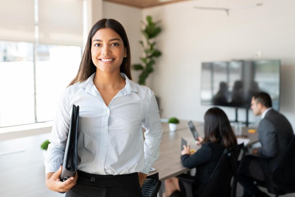 entrepreneurship development and business communication - a businesswoman standing in her office holding a file and smiling 
