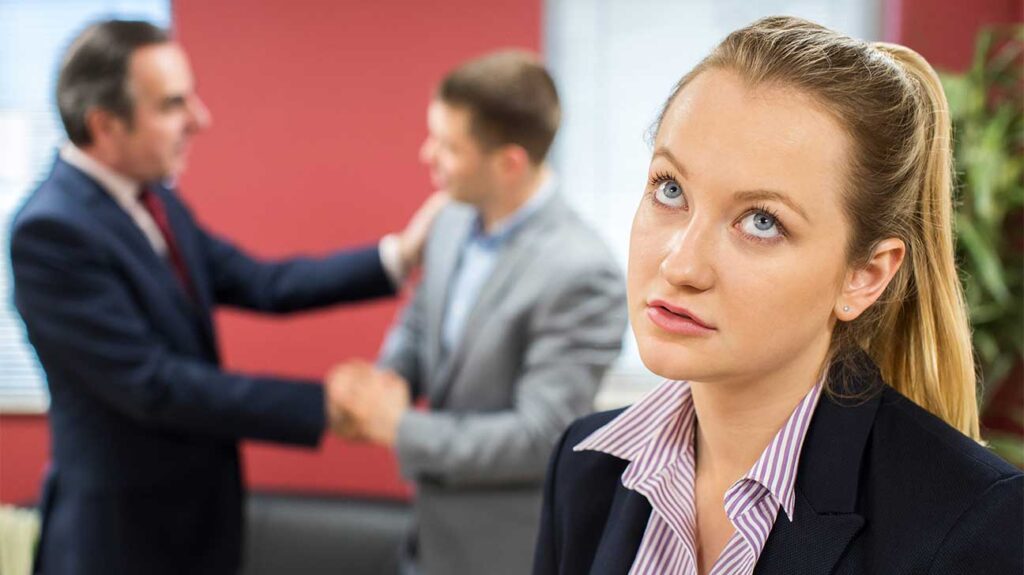 a manager promoting a man in the background and a women standard in front, looking distressed - problems of women entrepreneurship 